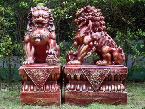Two red dragon dogs on top of decorated stone plinths.